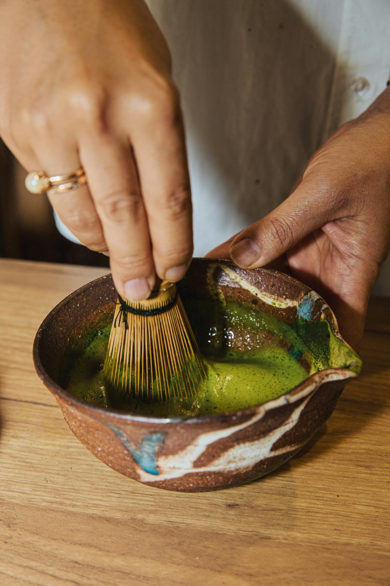 Hands whisking matcha in a rustic ceramic bowl.