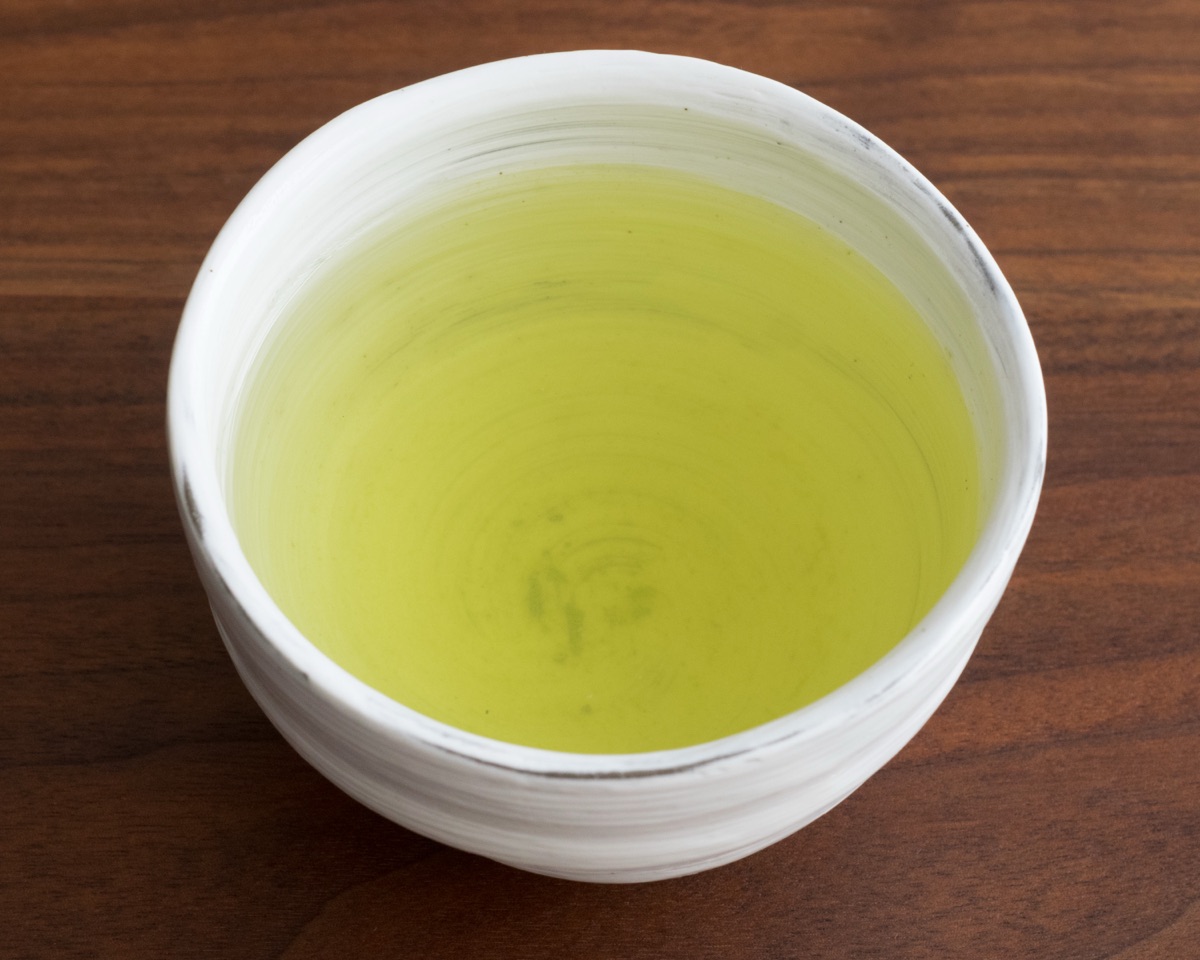 Sencha in a white ceramic cup on a wooden table. An illustrative tea photograph.